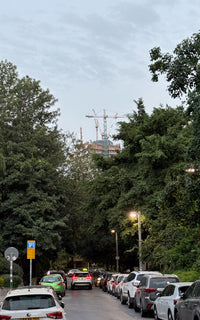 Street scene with cars parked along a tree-lined road, construction crane in the background.