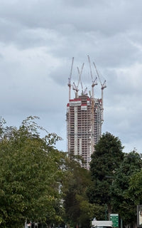 Quiet street in TLV center with tall building under construction with cranes against a cloudy sky appearing above.